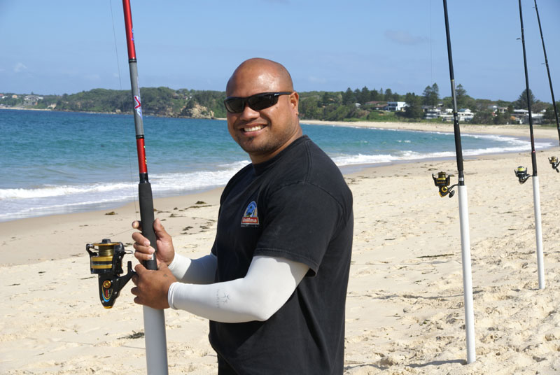A man standing on the beach beside fishing poles wearing IceRays Sun Sleeves for Maximum sun protection while fishing.